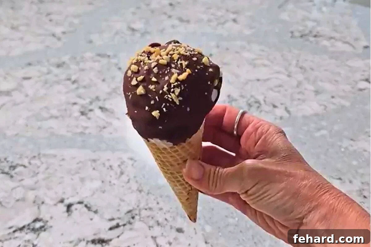 Coating Drumstick Cone with Chocolate and Peanuts Ice cream cone dipped in chocolate and coated in chopped nuts, ready to freeze.