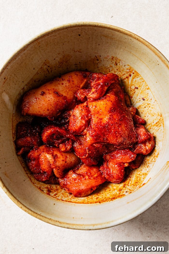 Raw, seasoned chicken thighs in a mixing bowl, ready for grilling