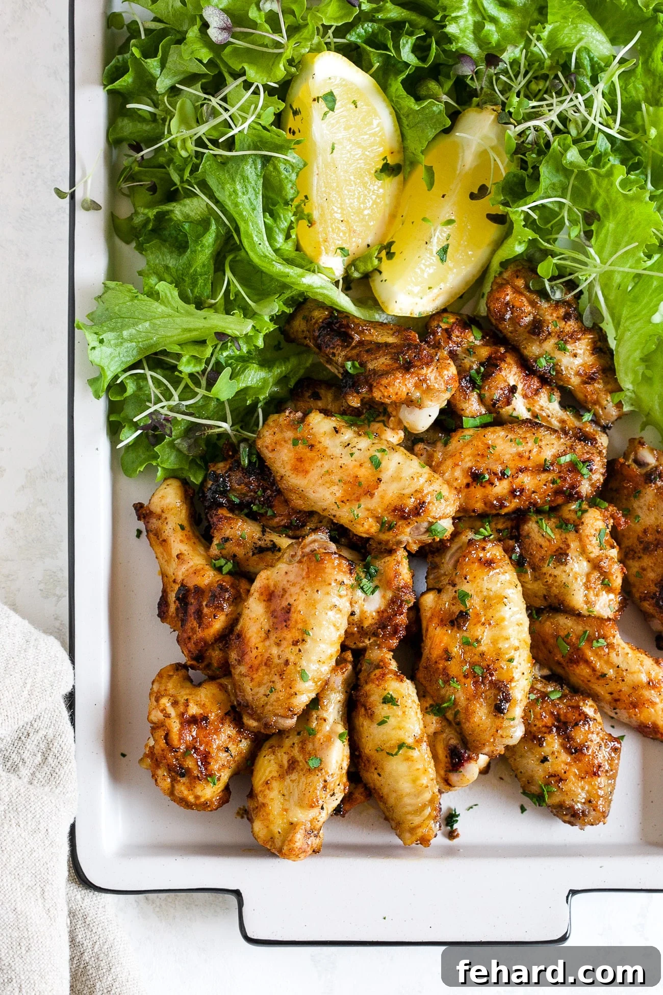 Crispy grilled chicken wings served on a white platter with fresh greens and lemon slices