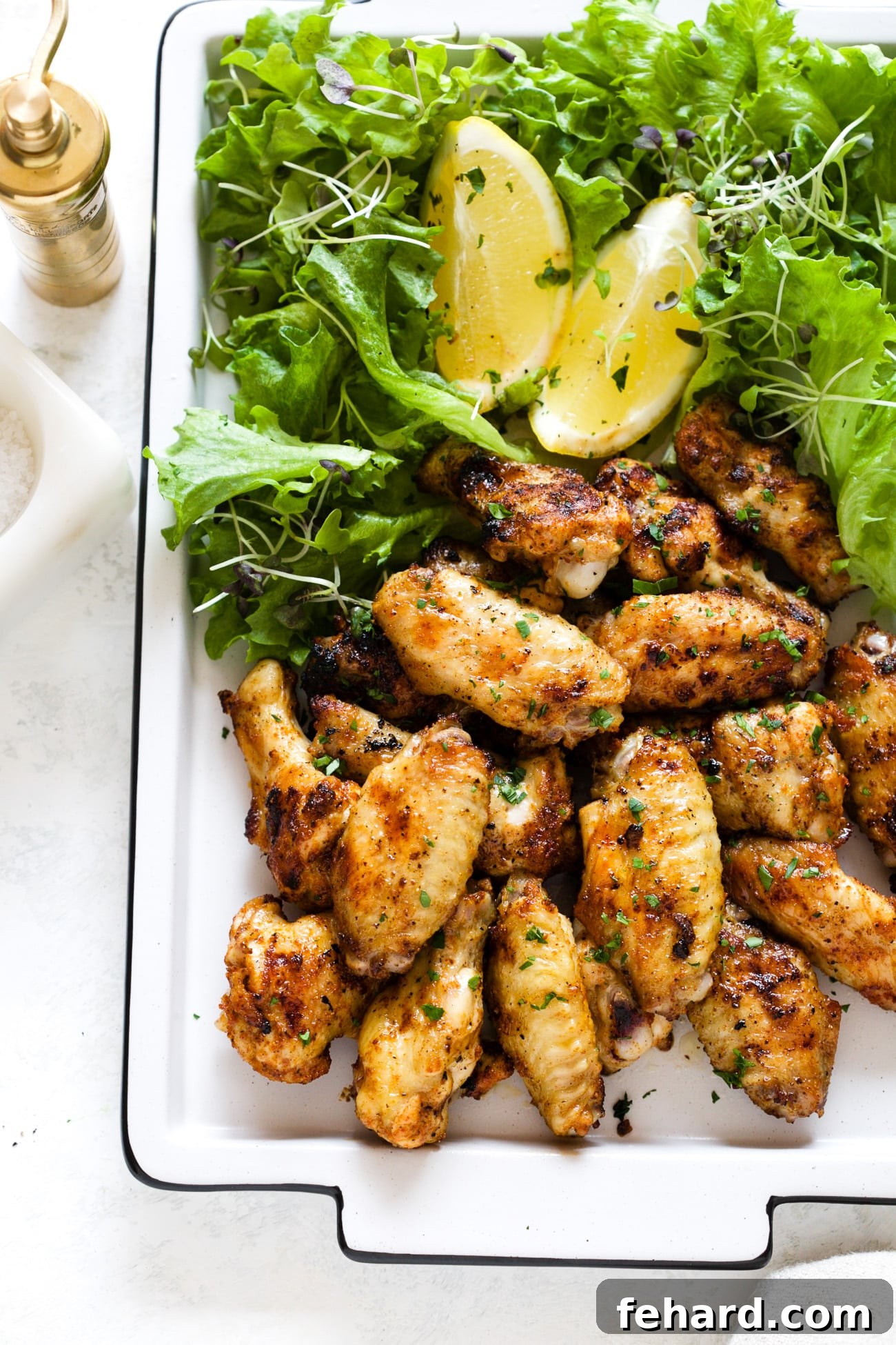 Crispy grilled chicken wings served on a white platter with fresh greens and lemon slices