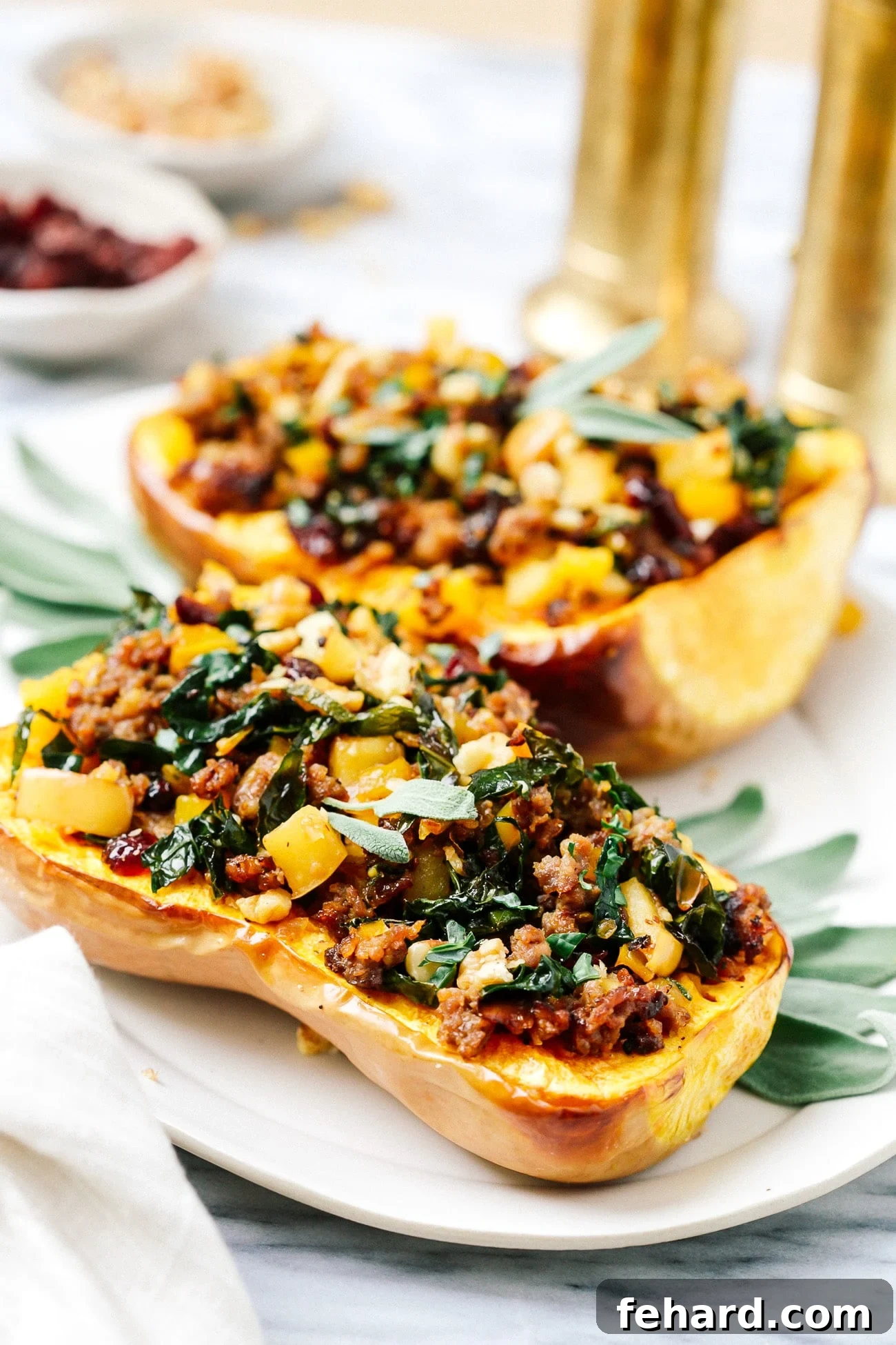 Two halves of golden-roasted stuffed butternut squash on a white serving plate, garnished with fresh sage.