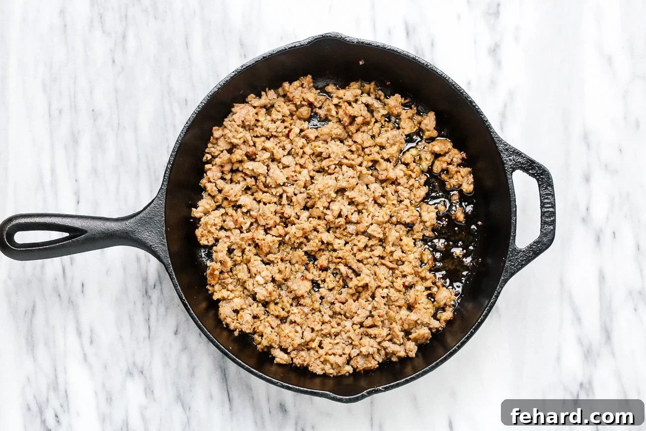 Crumbled and browned Italian sausage cooking in a cast iron skillet on the stovetop.