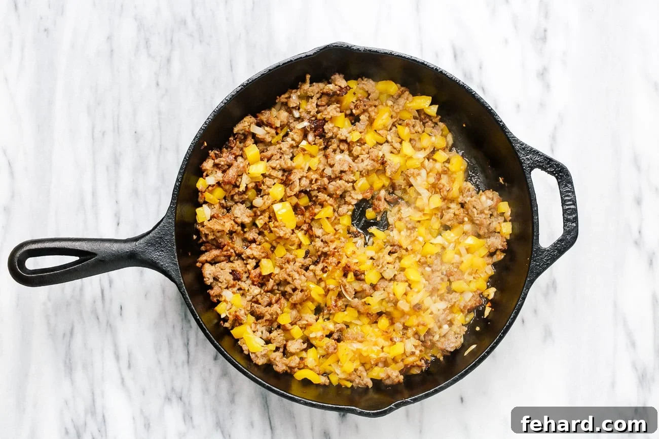 Diced onion, minced garlic, and diced yellow bell pepper added to the browned Italian sausage in a skillet.