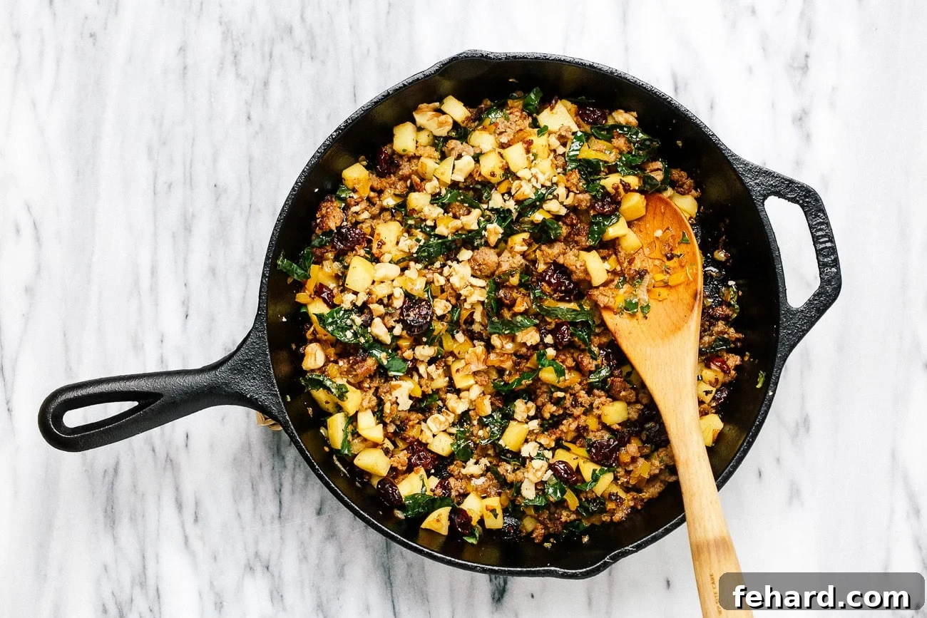 Dried cranberries and chopped walnuts fully mixed into the savory filling within the skillet.