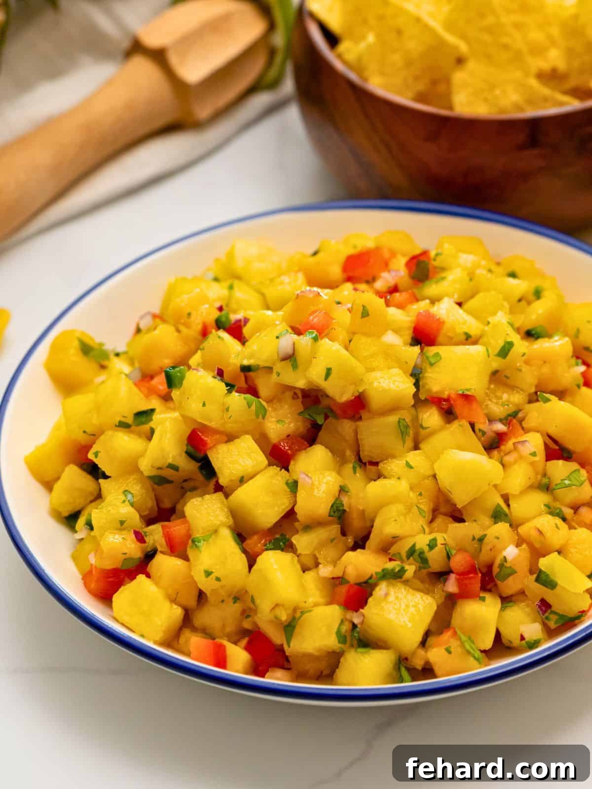 A beautifully arranged bowl of vibrant pineapple mango salsa, generously garnished with fresh cilantro, positioned next to a stack of crispy golden tortilla chips, inviting you to dive in.