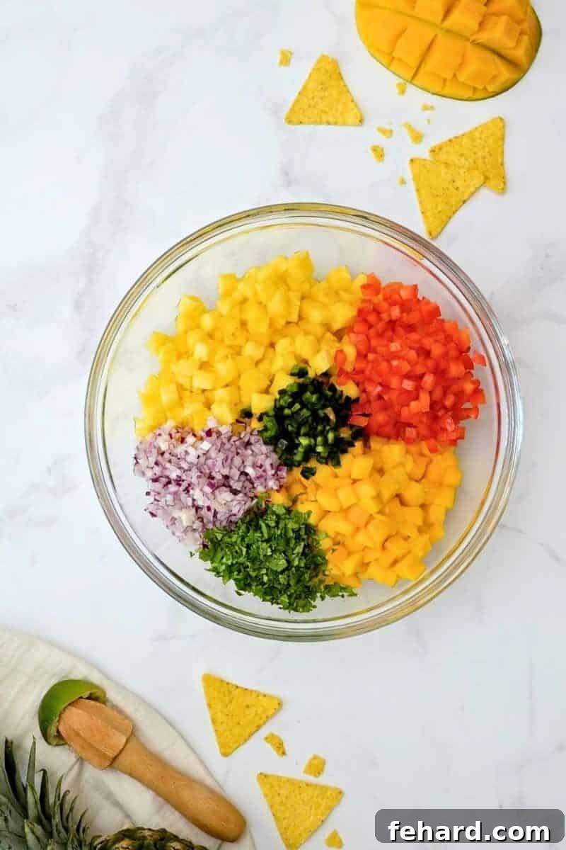 A large mixing bowl showcasing all the vibrant, freshly diced ingredients for pineapple mango salsa including pineapple, mango, red bell pepper, jalapeño, and cilantro, prior to being mixed with lime and salt.