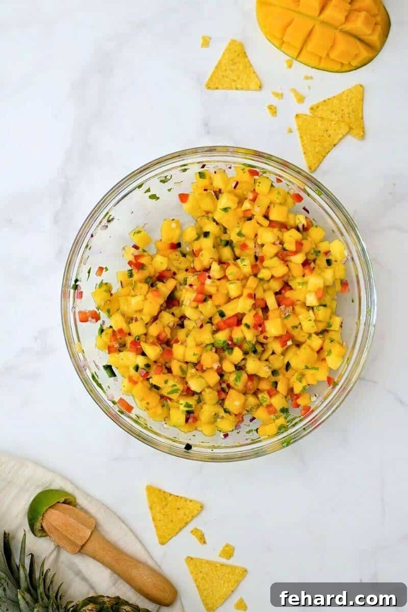 The same mixing bowl, now showing the diced pineapple mango salsa ingredients perfectly tossed and coated with lime juice and seasoning, displaying a vibrant and appealing texture.