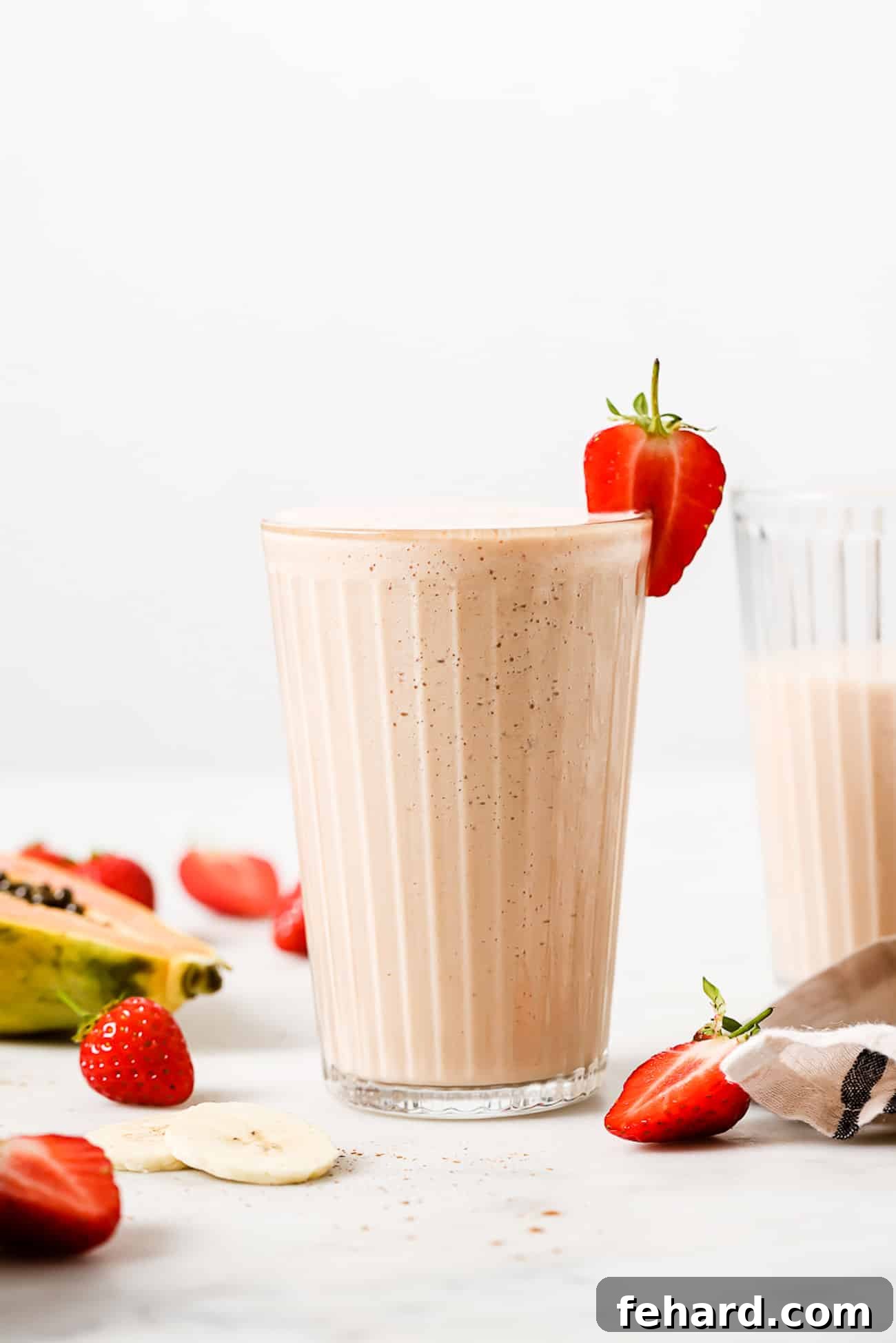 A papaya smoothie in a tall glass garnished with a strawberry slice.