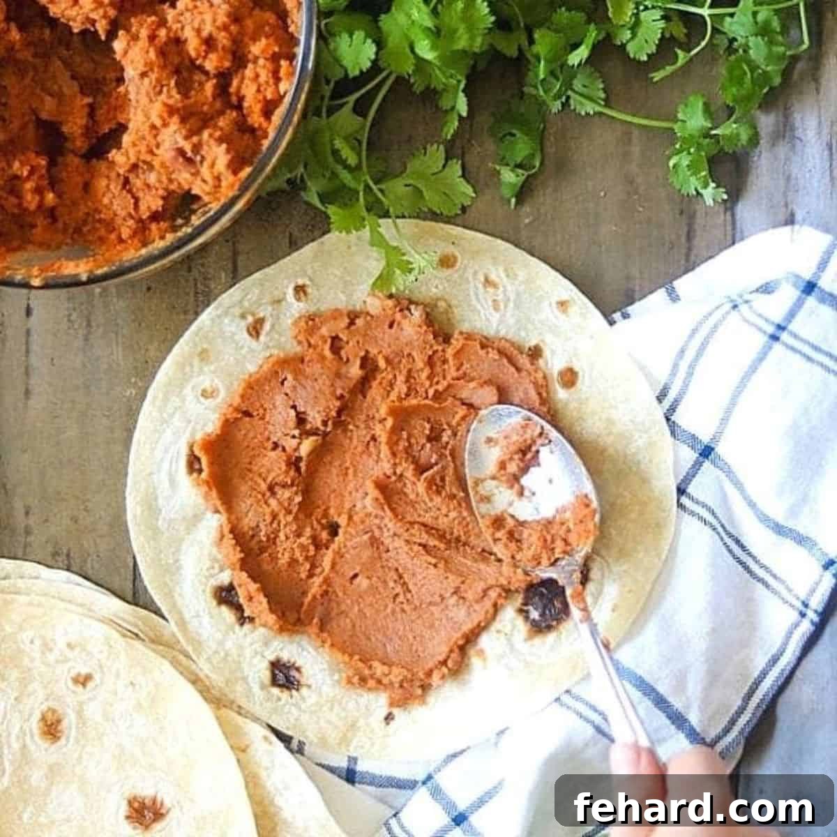 Refried beans being smoothly spread onto a tortilla, illustrating a simple and fast dinner idea.