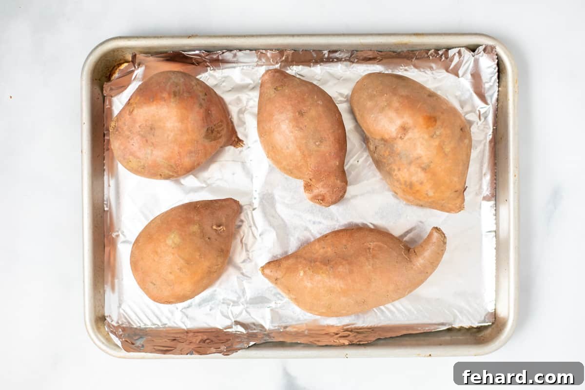 Velvety Homemade Sweet Potato Puree 3 Raw sweet potatoes arranged on a foil-lined baking sheet, ready for oven roasting.
