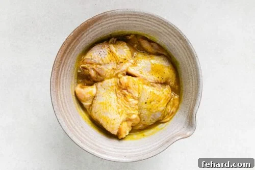 Raw chicken thighs with Dijon dressing arranged in a baking dish, covered with foil.