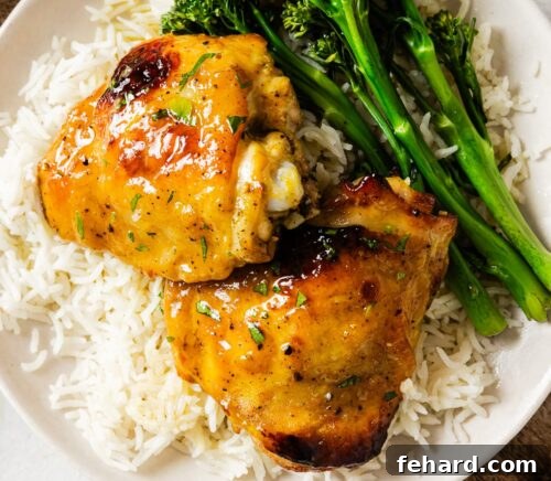 Dijon Chicken thighs served on a plate with rice, garnished with fresh herbs.