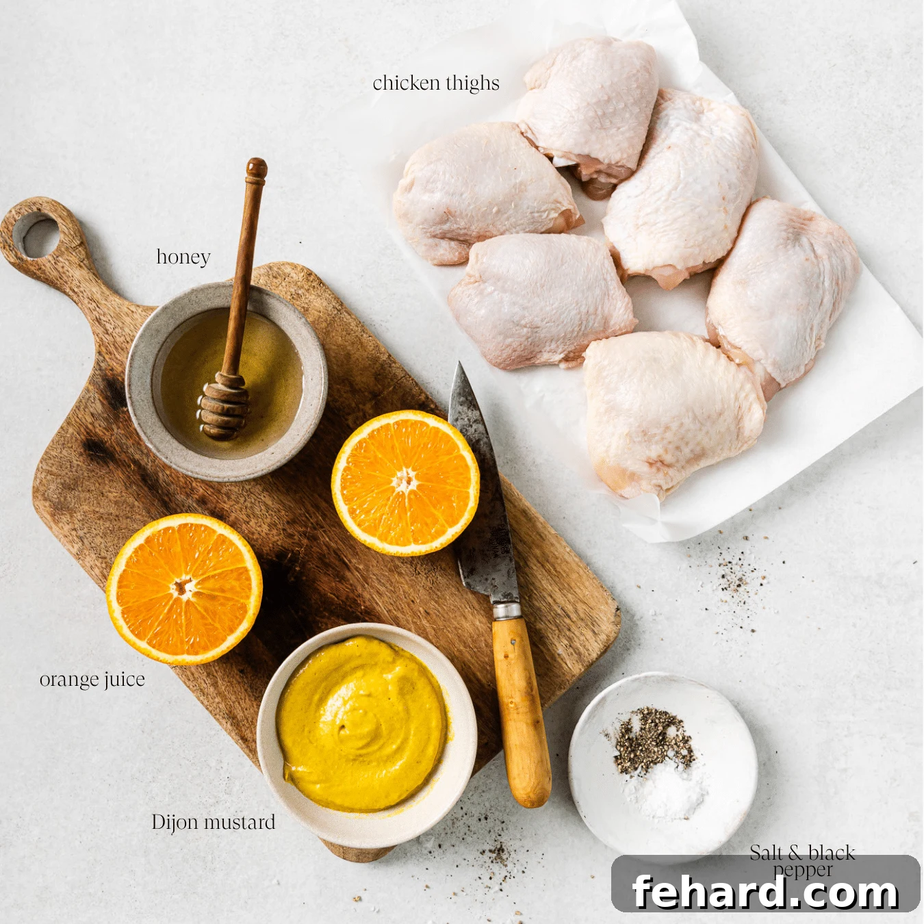 A collection of fresh ingredients on a kitchen countertop, including chicken thighs, Dijon mustard, honey, and oranges, ready for cooking.