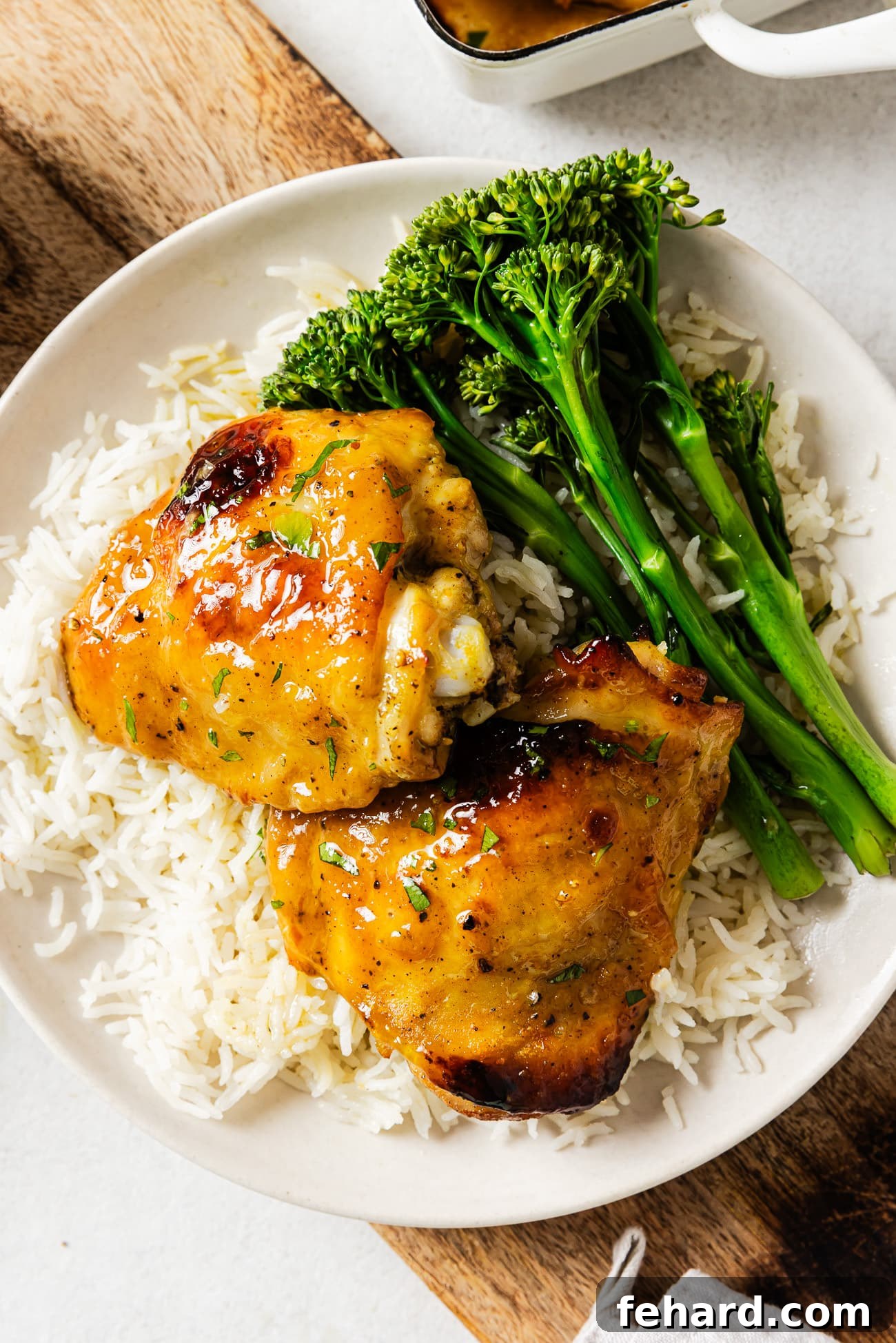 A plate featuring two baked Dijon chicken thighs, served alongside fluffy white rice and garnished with fresh parsley.