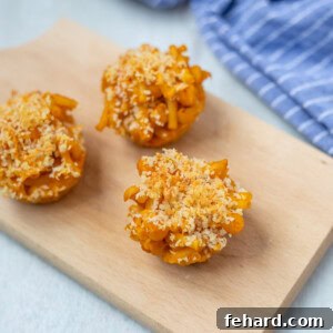 Three golden Mac and Cheese Muffins on a wooden cutting board, ready for serving.