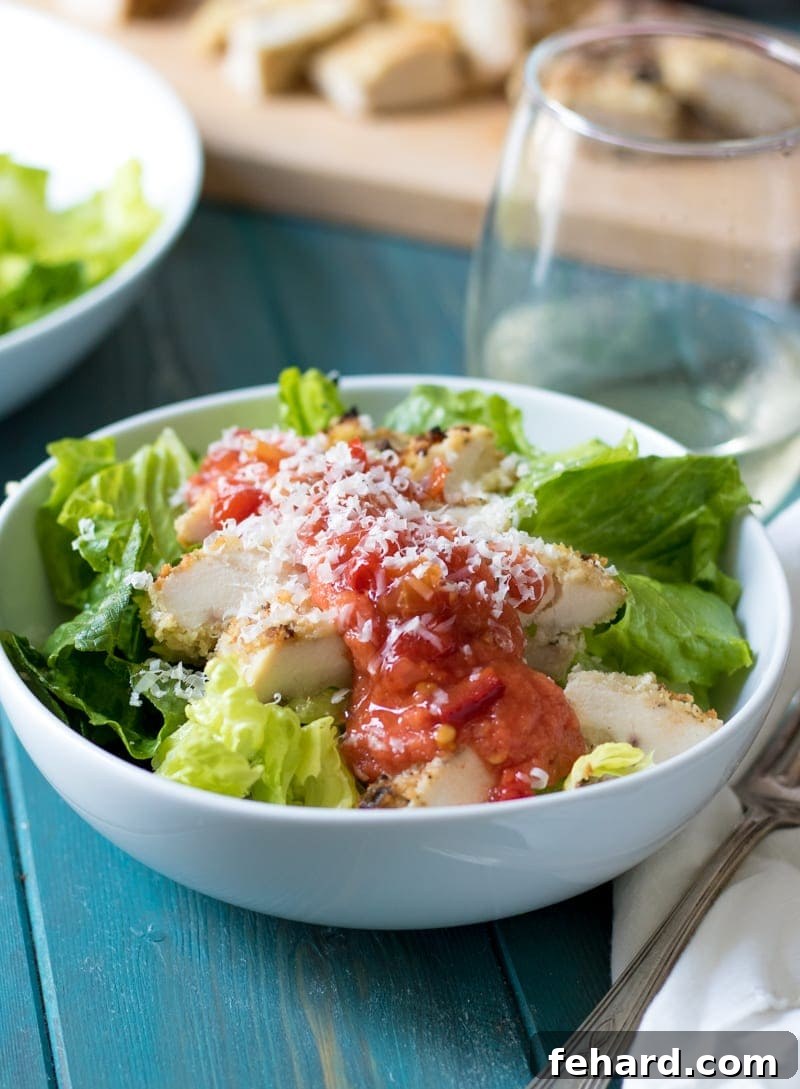 A vibrant bowl of fresh Chicken Parmesan Salad featuring crisp romaine lettuce, golden-brown crispy chicken tenders, rich red marinara sauce, and a generous sprinkle of Parmesan cheese.