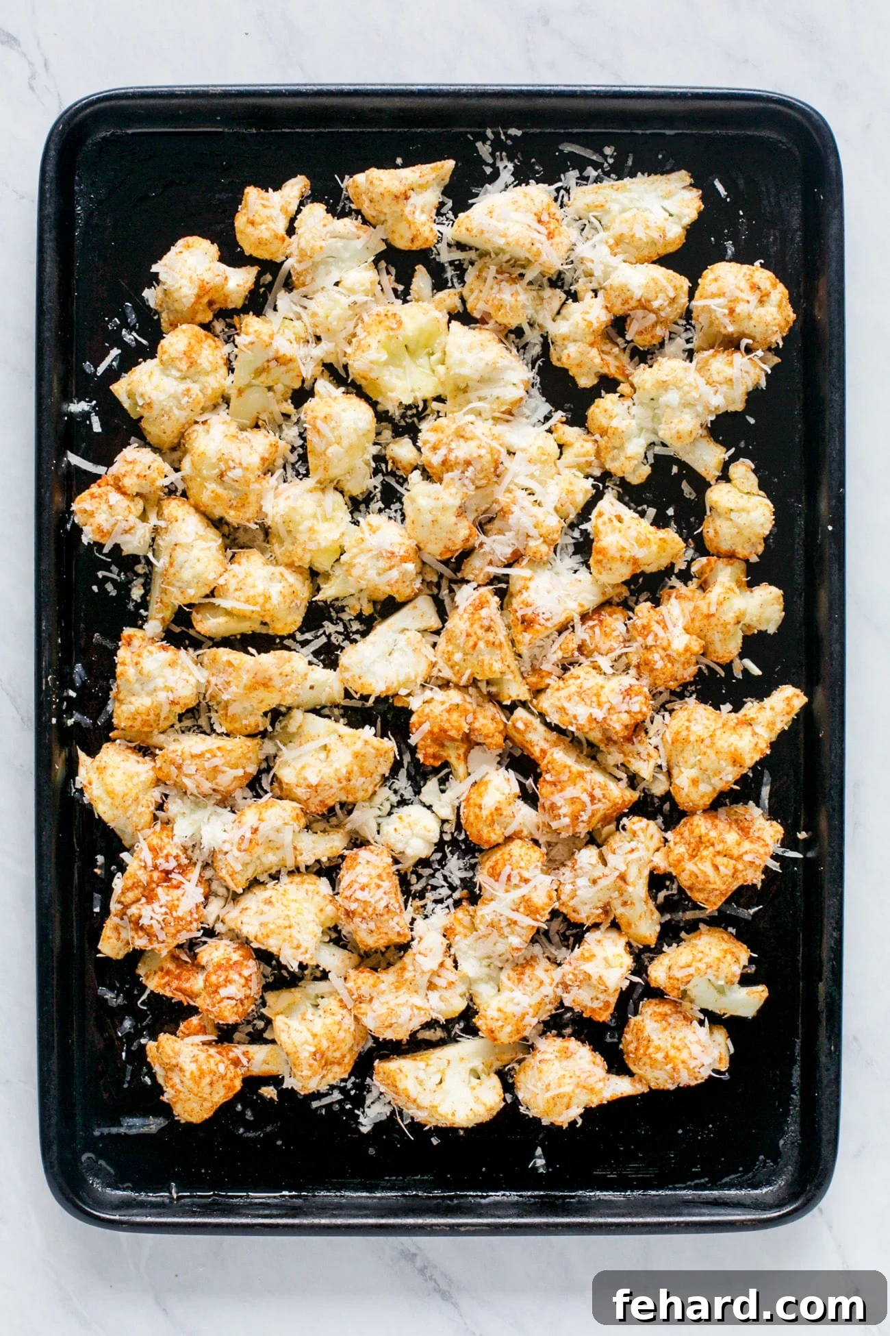 Crispy Cauliflower Poppers 5 Roasted cauliflower florets arranged in a single layer on a parchment-lined baking sheet, showing golden-brown edges.