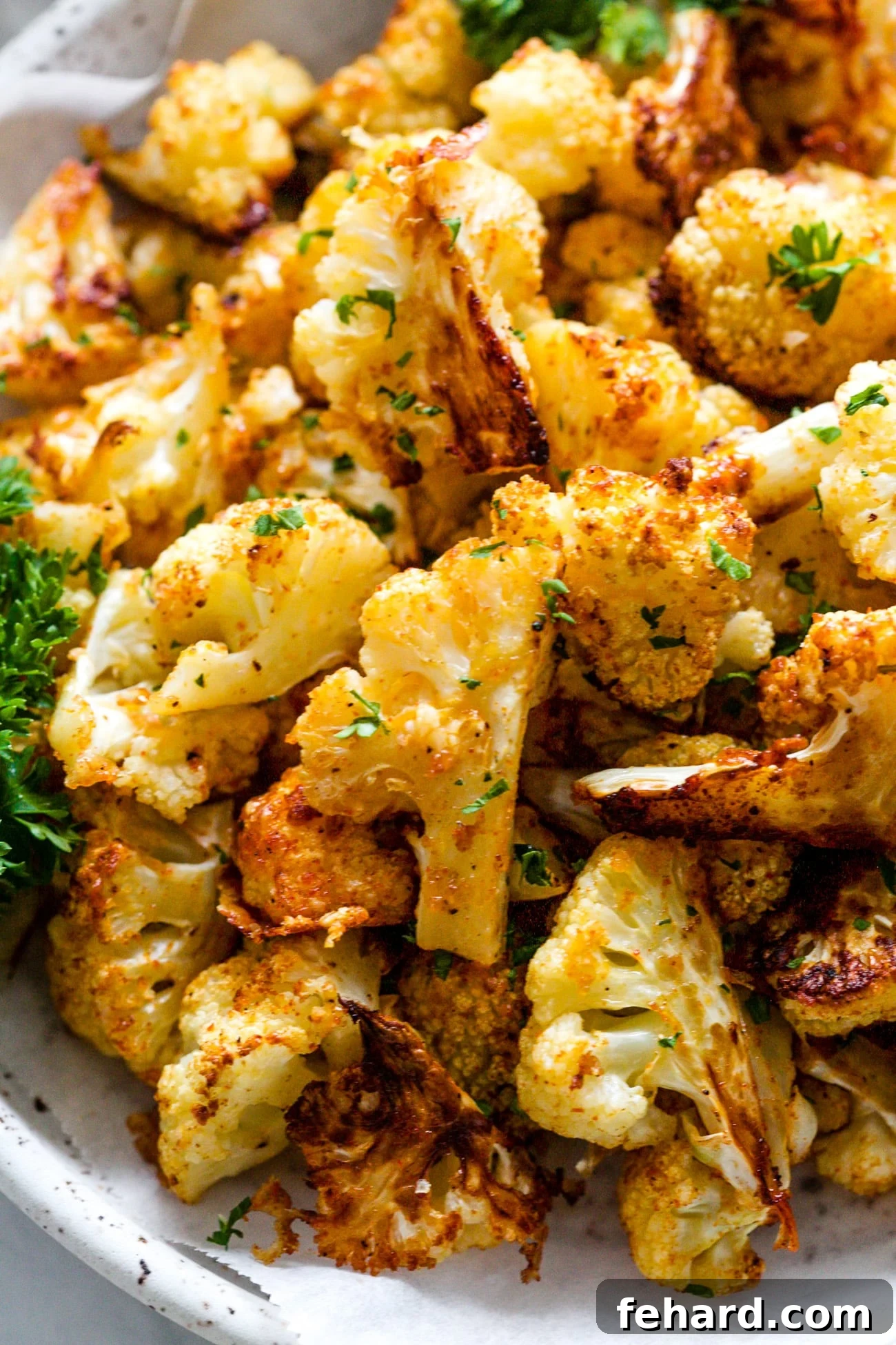 Crispy Cauliflower Poppers 6 Close-up shot of crispy, golden-brown cauliflower bites in a white serving dish, garnished with fresh green parsley.