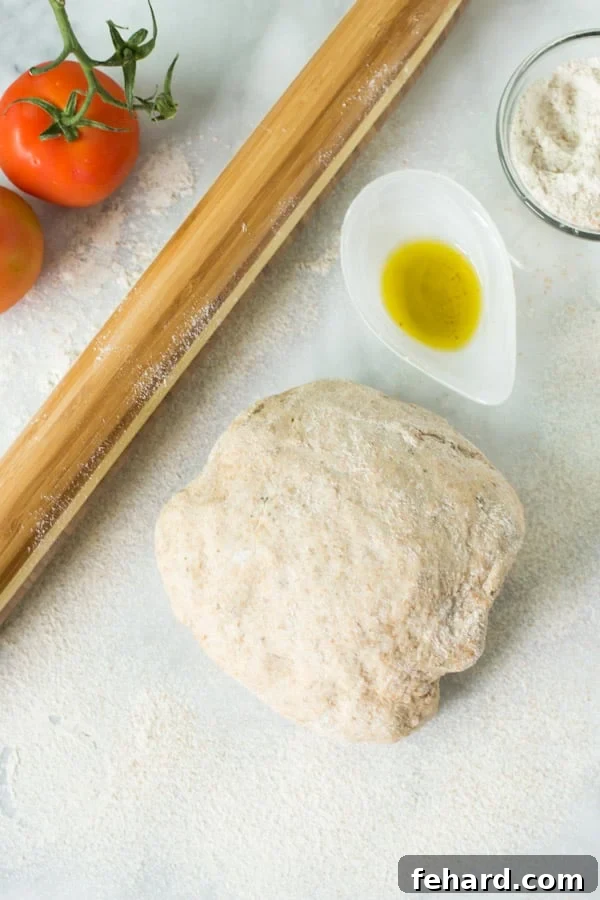 Flavorful whole wheat pizza dough ready for baking, alongside a rolling pin and olive oil
