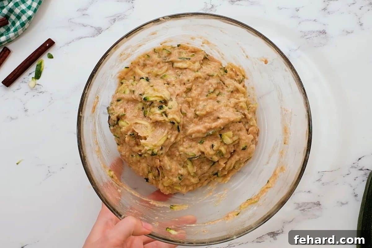 A mixing bowl filled with thick, moist zucchini bread batter, featuring visible shreds of zucchini and bright pieces of crushed pineapple, ready for its final fold.