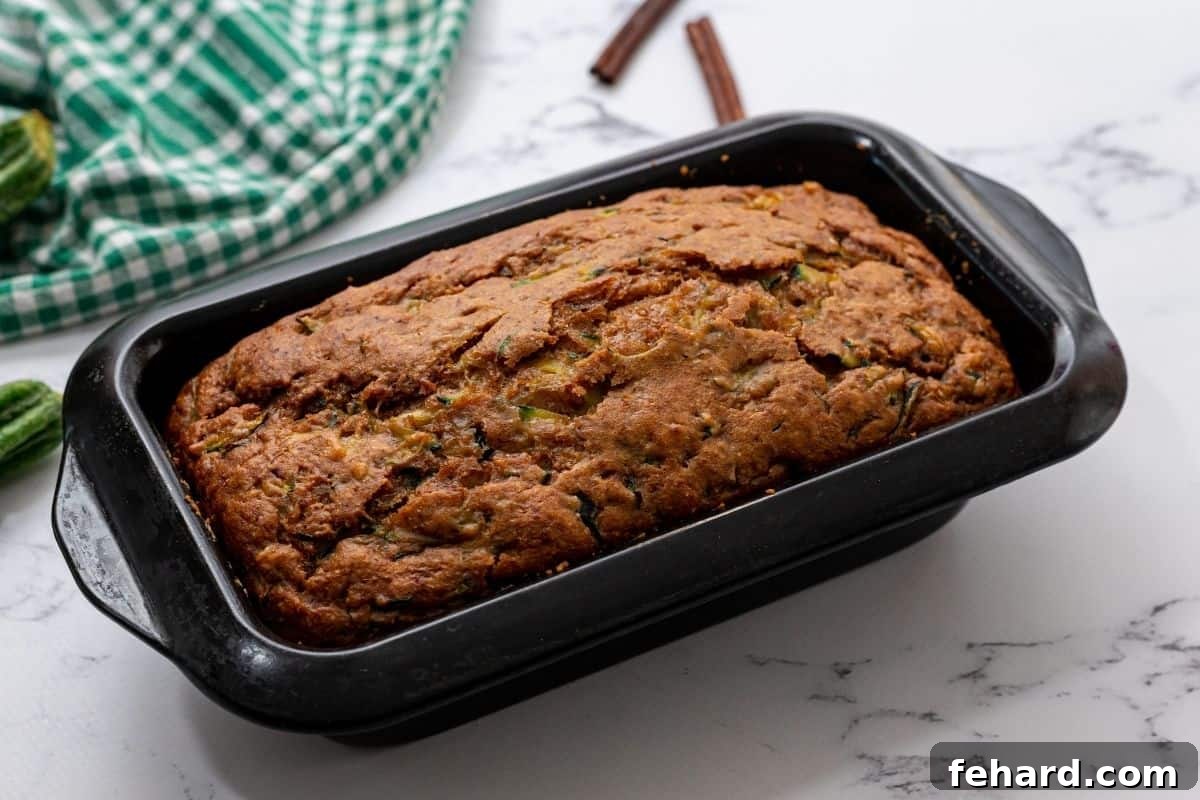 A perfectly baked loaf of pineapple zucchini bread, with a rich golden-brown top, sitting in its loaf pan on a cooling rack, freshly out of the oven.