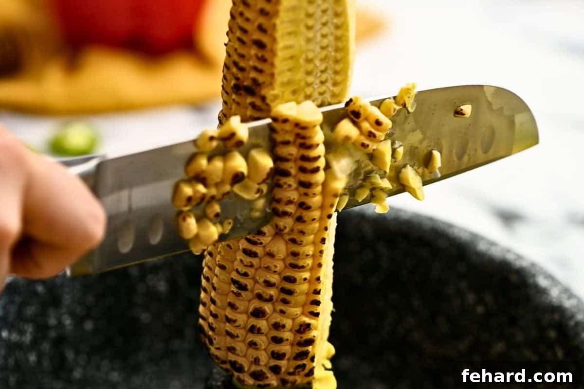 How to Cut Corn off the Cob A chef's knife carefully slicing corn kernels off the cob directly into a Bundt cake pan for easy collection.