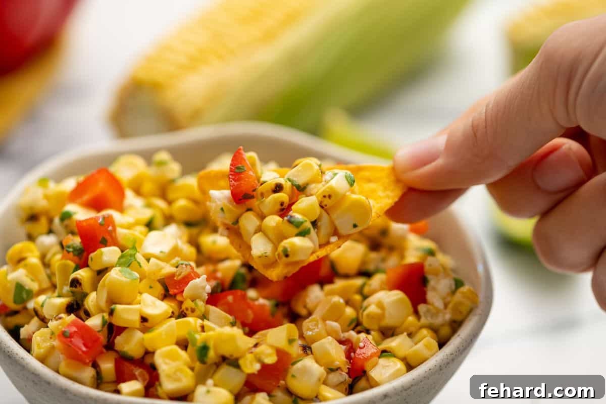 Best Corn Salsa Served with Chips A tortilla chip generously scooping up a portion of the delicious grilled corn salsa, ready to eat.