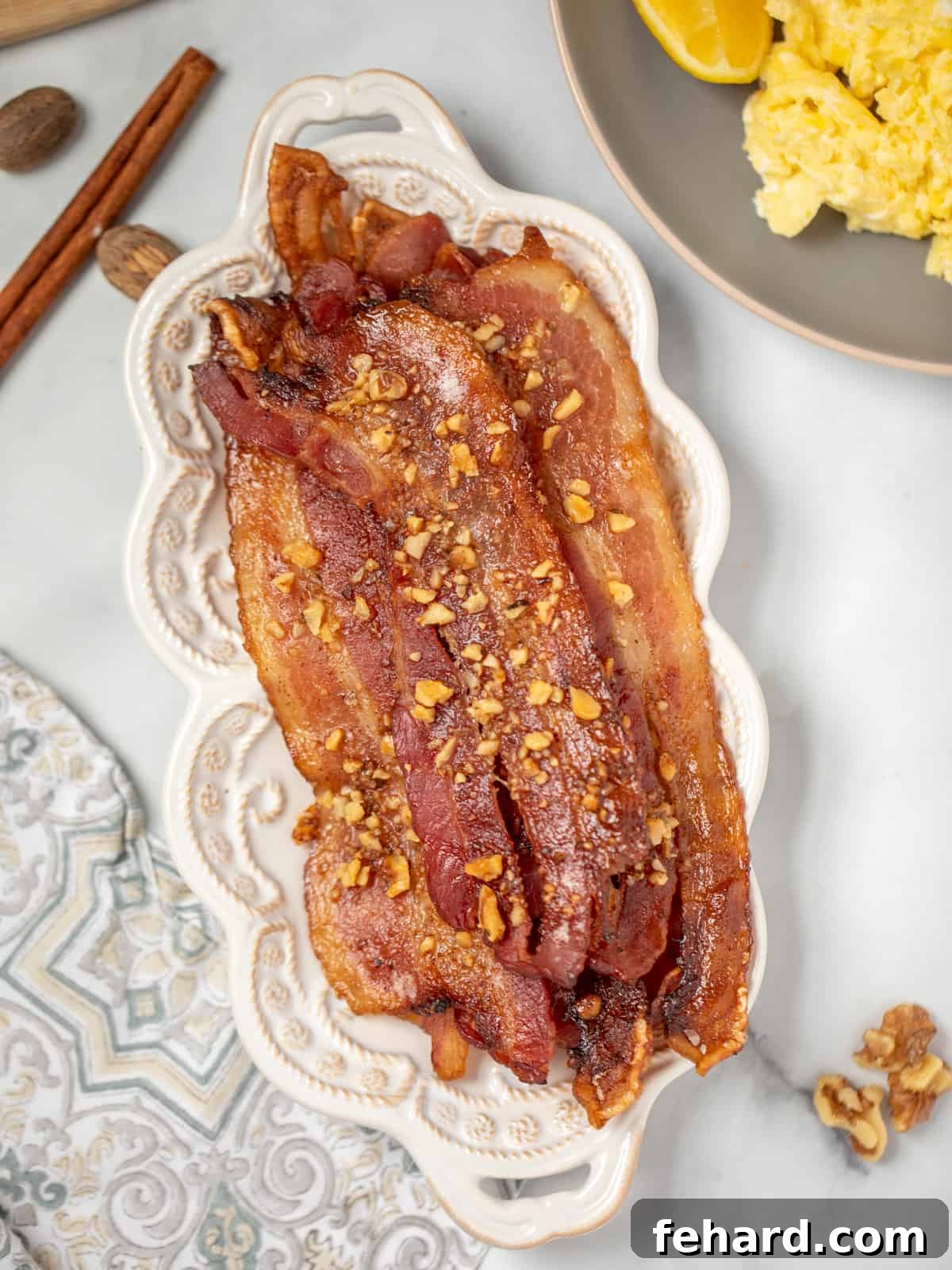 Crispy Candied Maple Bacon on a white serving platter, beautifully arranged next to fluffy scrambled eggs, highlighting its golden-brown, glazed perfection.