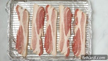 Raw bacon strips neatly arranged in a single layer on a baking sheet with a rack, ready for glazing.