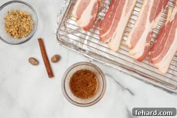 A small bowl of maple glaze mixed with spices sits beside raw bacon on a sheet pan, ready for application.