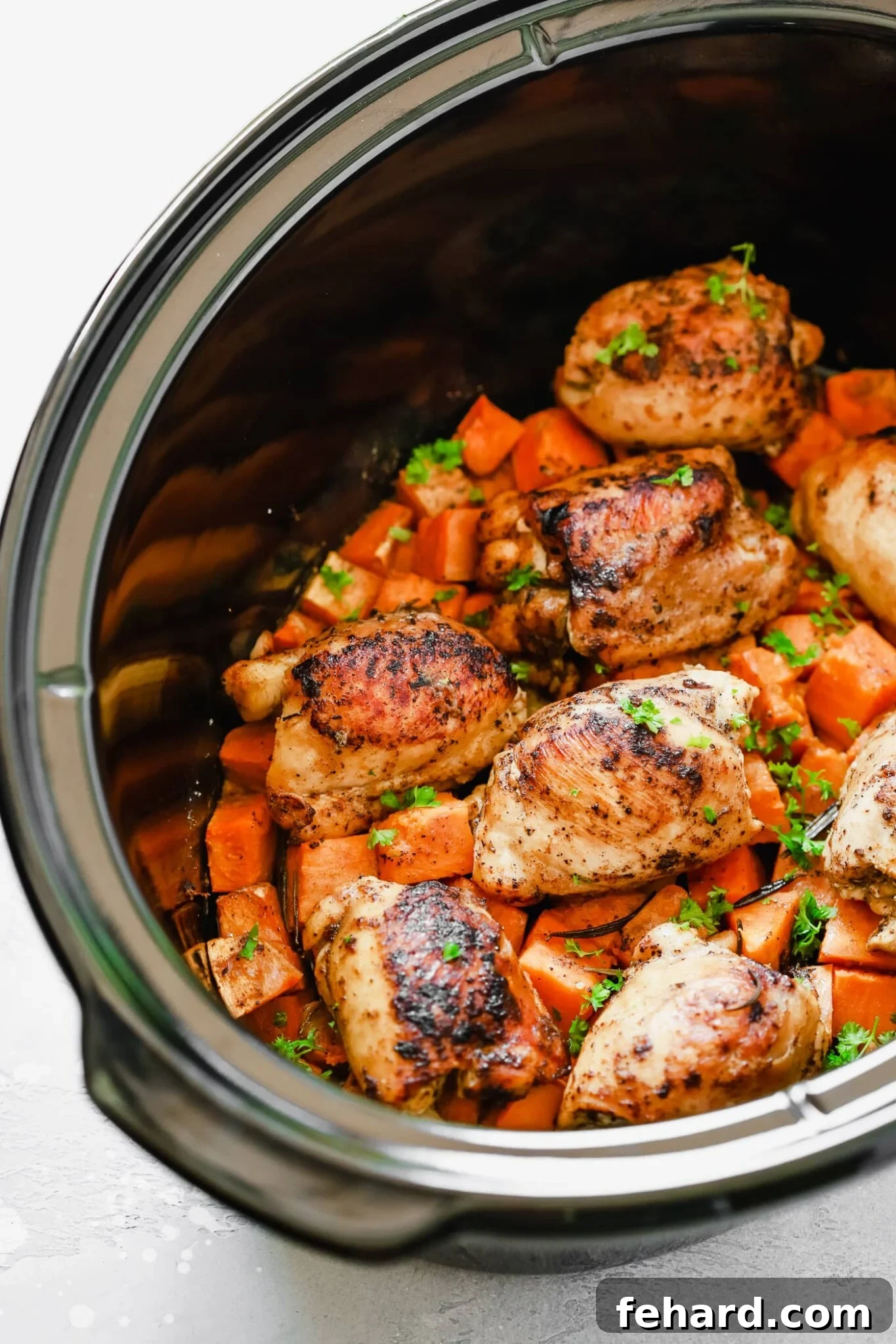 overhead view of a slow cooker pot containing sweet potato and chicken, garnished with fresh herbs