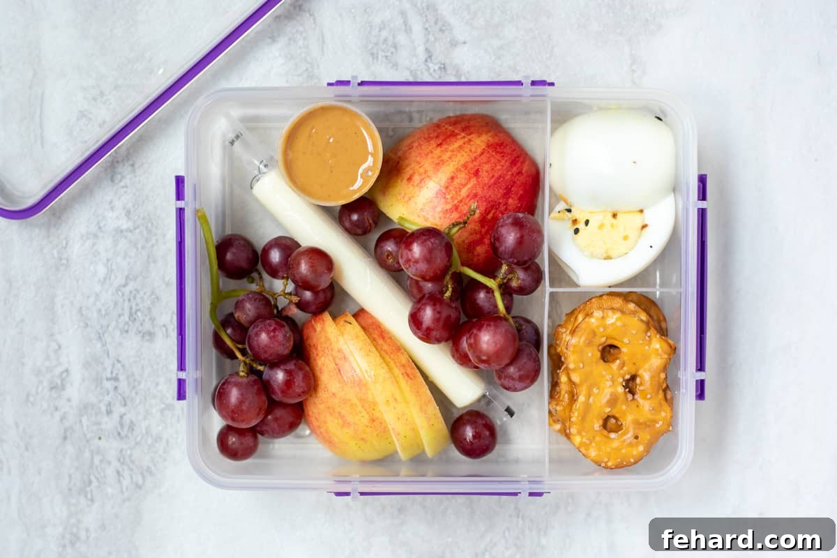 Lunch container with sliced apples, grapes, peanut butter, cheesestick, pretzels, and hard boiled eggs.