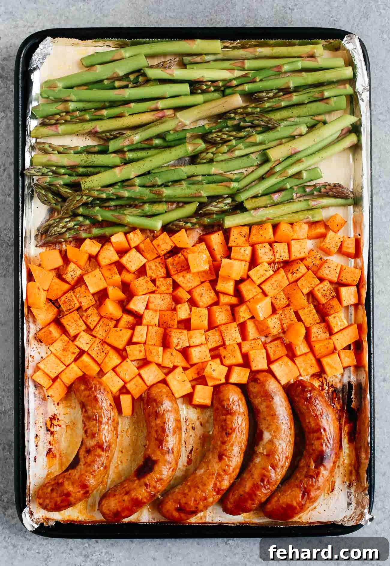 A sheet pan with sausage, potatoes, and asparagus.