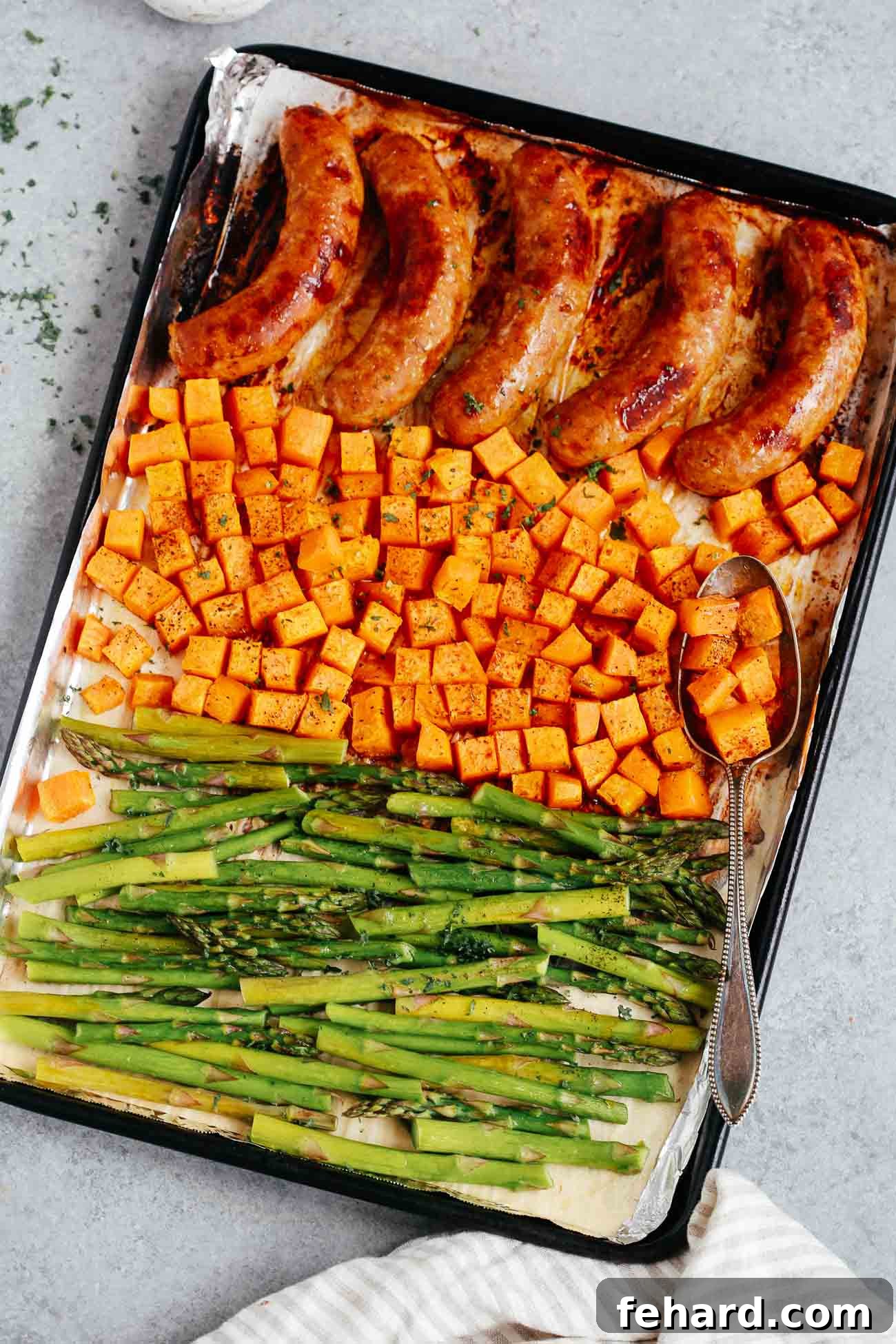 Overhead view of a sheet pan containing cooked sausage, sweet potatoes, and asparagus.