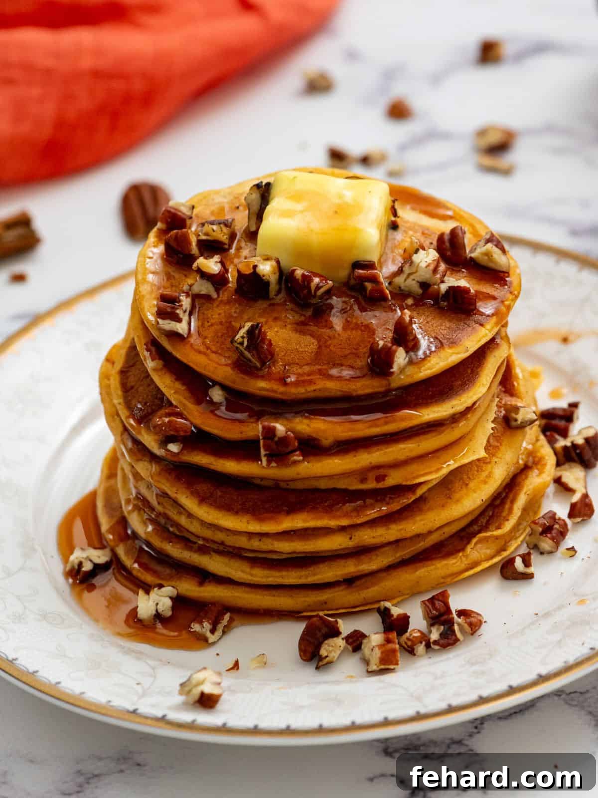 Stack of fluffy sweet potato pancakes on a plate, generously topped with maple syrup and chopped nuts.