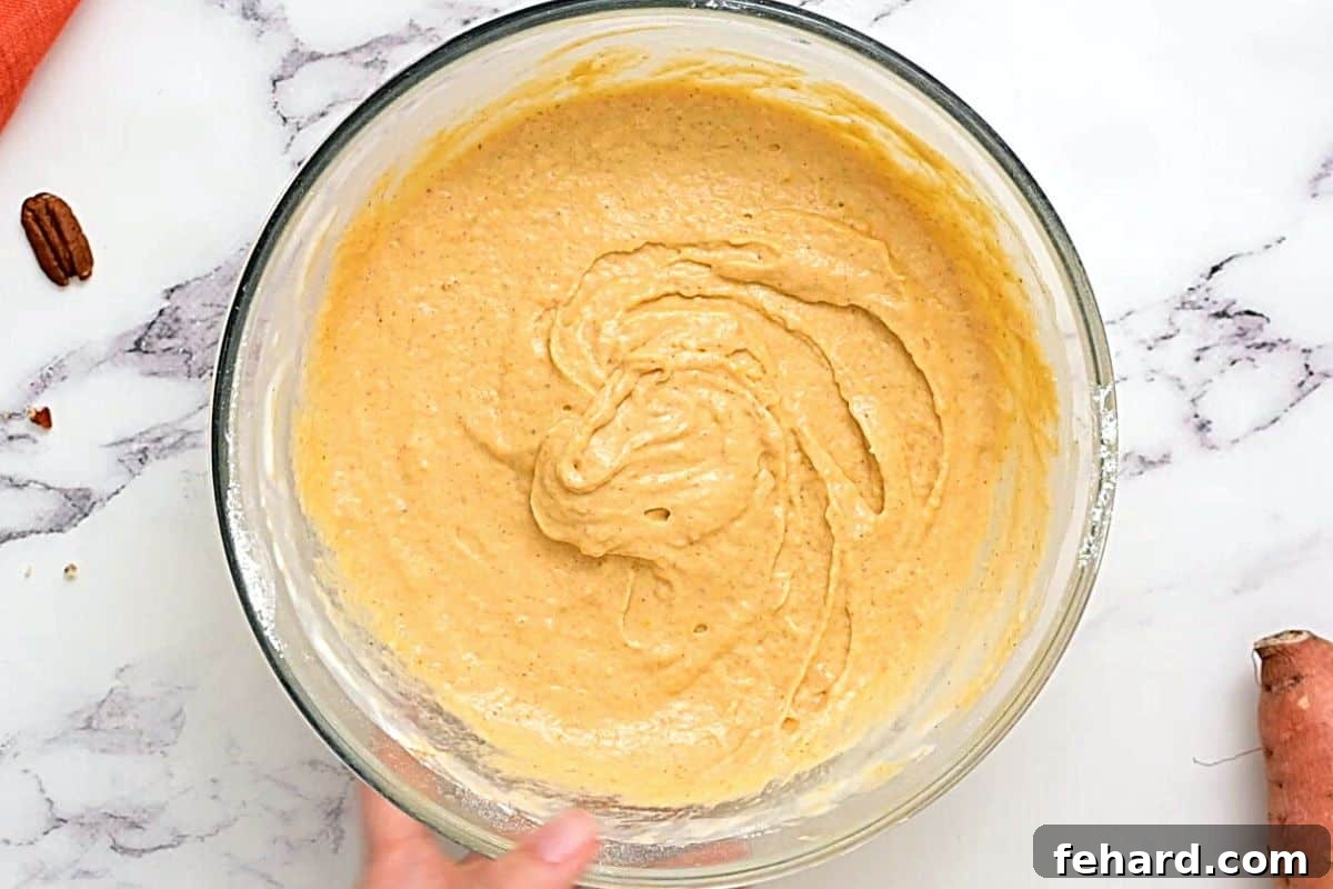 Thick, vibrant orange sweet potato pancake batter in a clear glass bowl, ready for cooking.