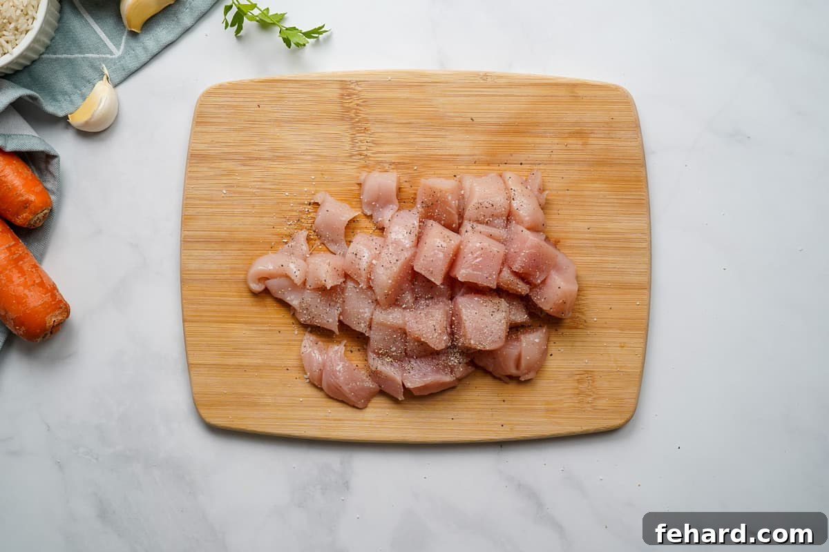 IP Chicken and Rice Diced boneless, skinless chicken on a cutting board, seasoned evenly with salt and pepper, ready for sautéing.