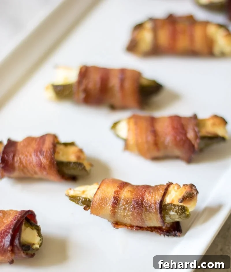 Bacon Wrapped Jalapenos Jalapeno Poppers filled in cream cheese and wrapped in bacon on white platter.