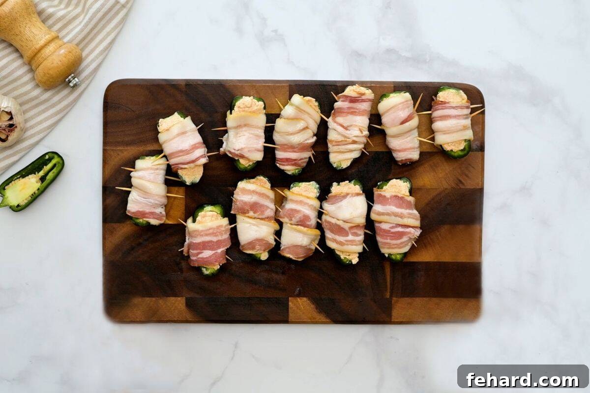 Jalapeno Popper with bacon Jalapenos stuffed with cream cheese and wrapped in bacon on cutting board.