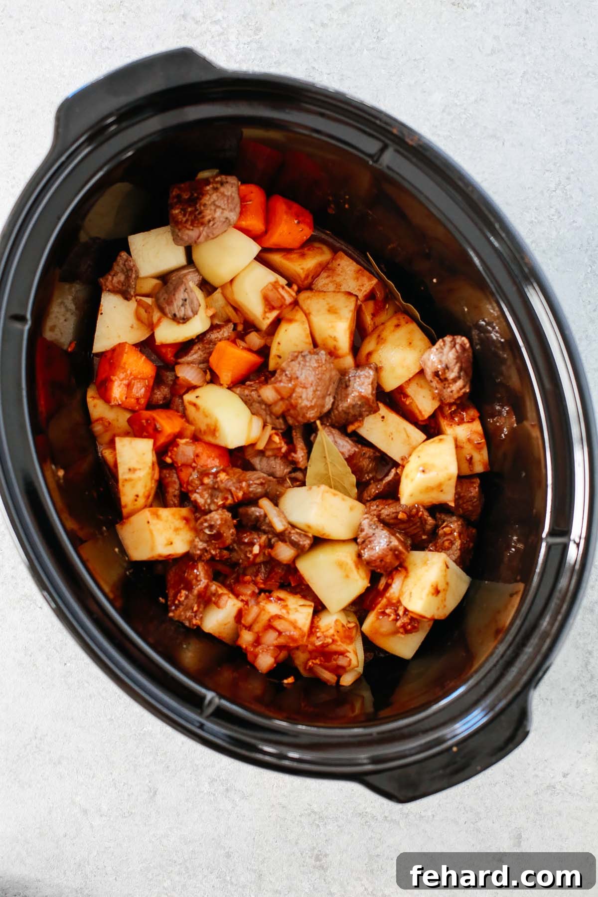 Overhead image of ingredients for the beef stew being adding to the slow cooker before cooking.