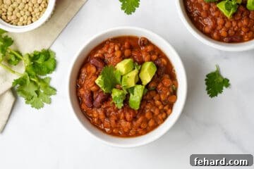 Lentil Chili dished up in white bowl topped with avocado and cilantro.