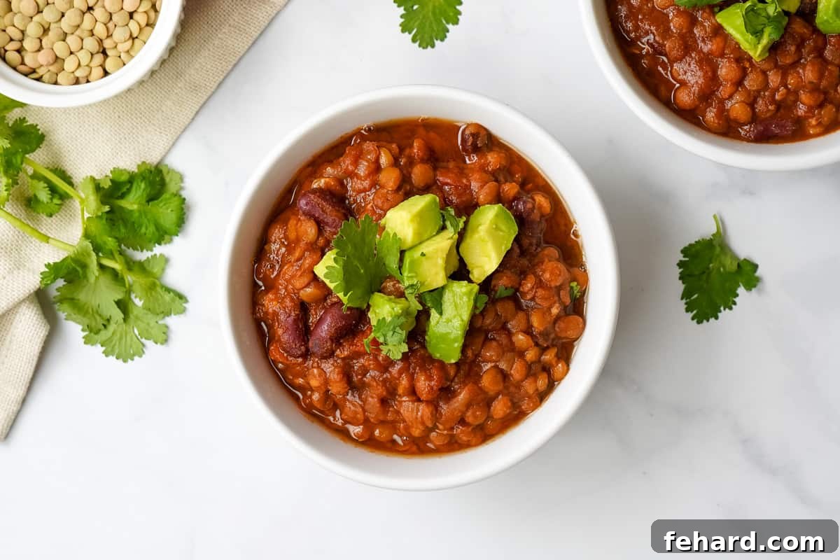 A white bowl brimming with Instant Pot Lentil Chili, elegantly topped with fresh avocado slices and vibrant cilantro.