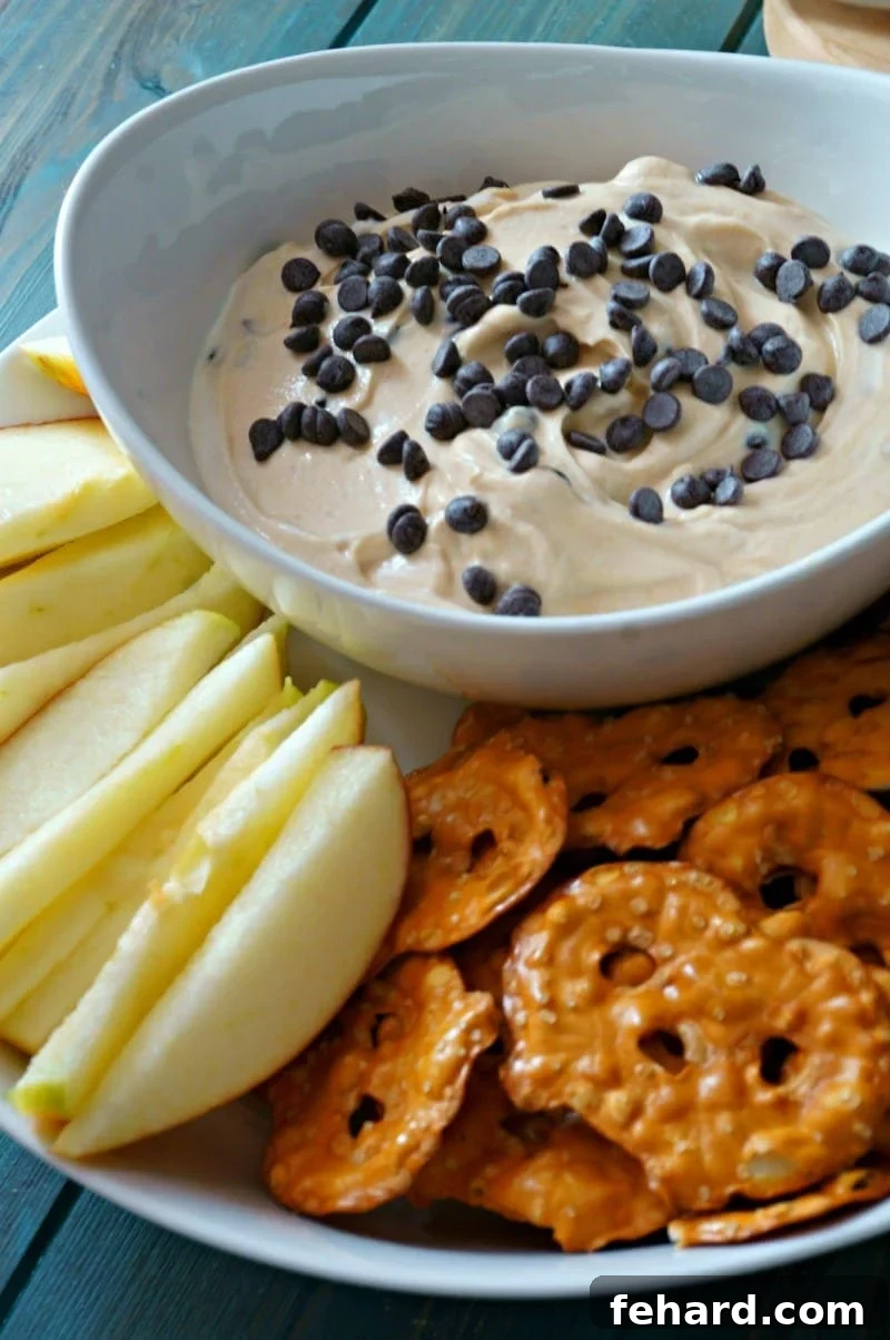 Creamy 5-Ingredient Chocolate Peanut Butter Yogurt Dip in a white bowl, surrounded by fresh apple slices and savory pretzels, perfect for dipping.