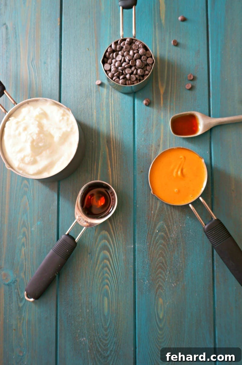 All 5 ingredients for Buckeye Dip: Greek yogurt, peanut butter, vanilla extract, maple syrup, and mini chocolate chips, laid out on a white surface.