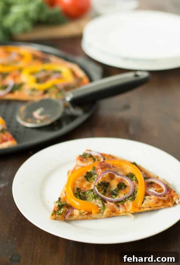 A perfectly baked slice of Kale, Peppers, Red Onion Pizza, showing a thin crispy crust and abundant toppings on a white plate