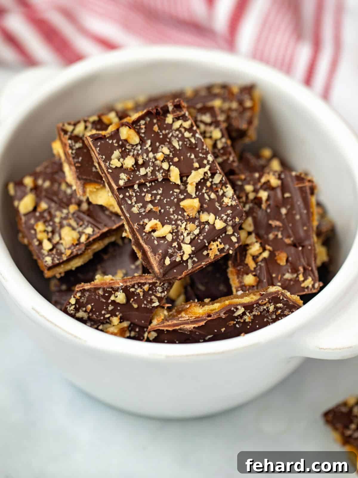 A bowl filled with golden Saltine Cracker Toffee pieces, garnished with chocolate and walnuts.
