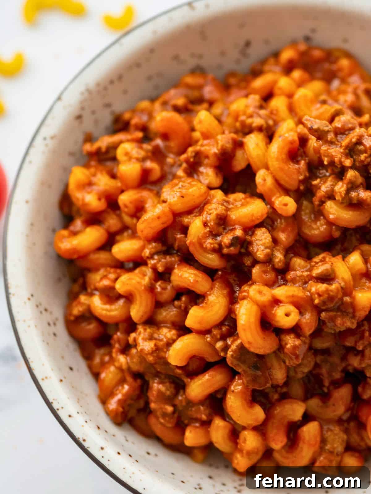 Homemade Hamburger Helper dished up in white dish showing ground beef and macaroni noodles coated with rich tomato sauce, garnished with fresh parsley.