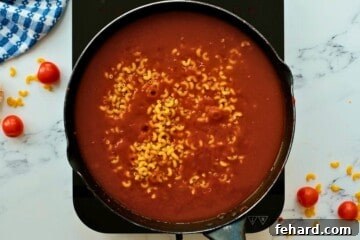 Elbow noodles added to a skillet with ground beef, beef broth, and tomato sauce for the hamburger helper recipe.