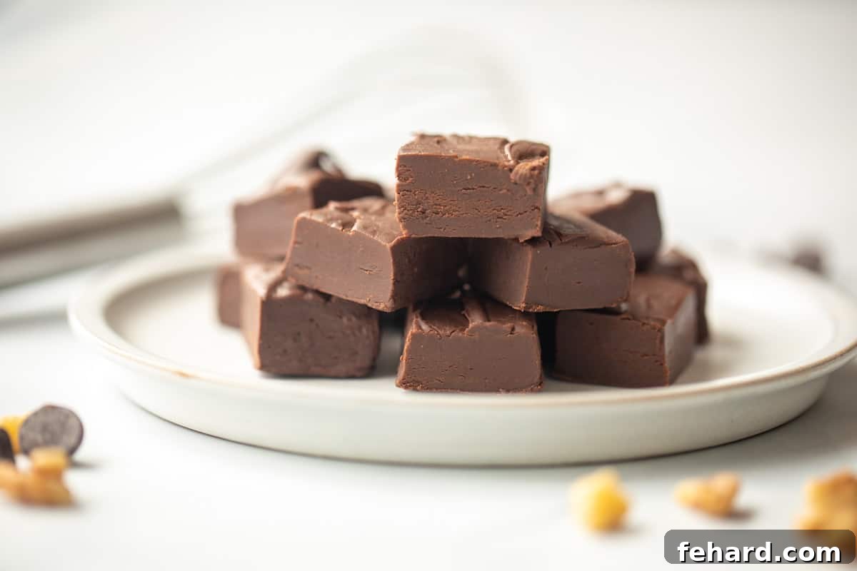 Delicious microwave fudge cut into neat cubes on a pristine white plate, with additional nuts and chocolate chips artfully scattered in the background, suggesting richness and flavor.