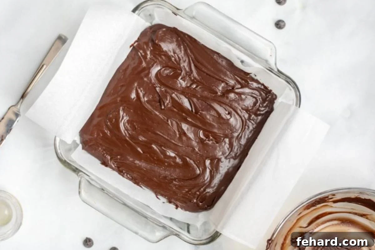 The smooth, dark chocolate fudge mixture neatly spread out in an 8-inch glass baking dish, lined with parchment paper, ready for chilling.